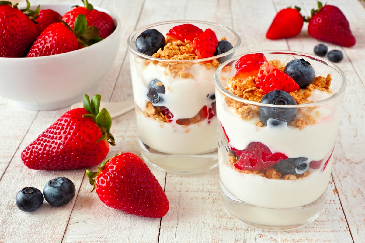 Two yogurt parfaits on a picnic tables surrounded by various berries.