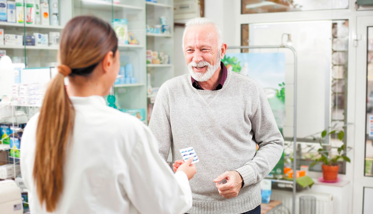 A pharmacist handing a senior patient a packet of pills.