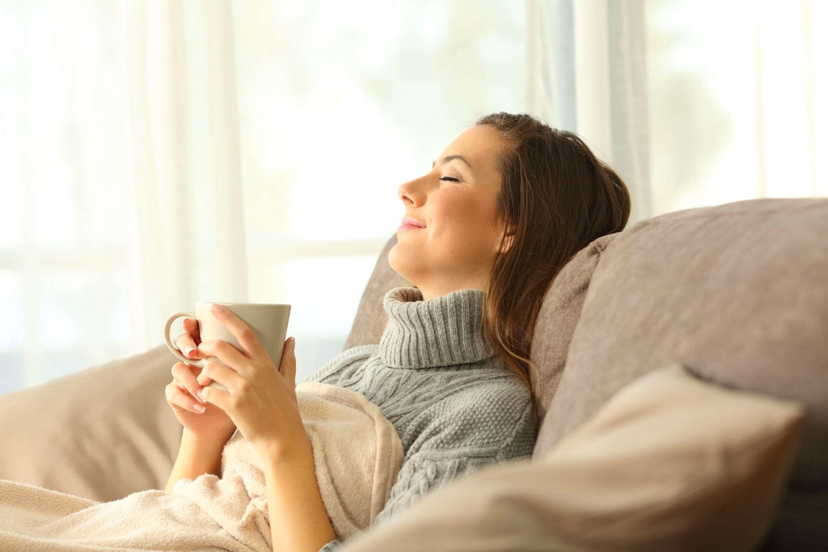 A woman relaxing on her couch with a blanket and mug of tea.
